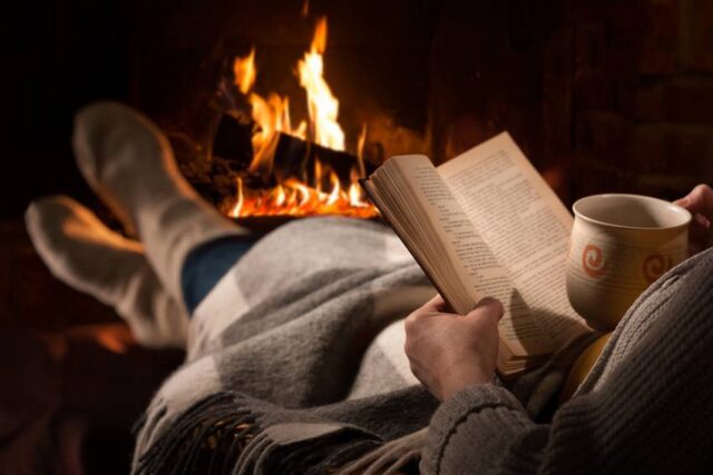 Woman Reads Book Near Fireplace